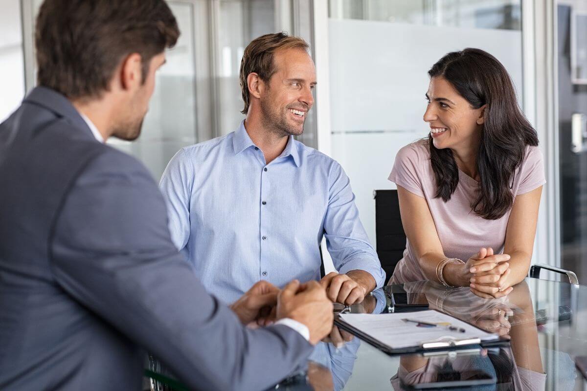 The image tells about a clipboard on the table, a couple, and a financial advisor in a suit which help clients plan for the future while earning over$50 an hour.