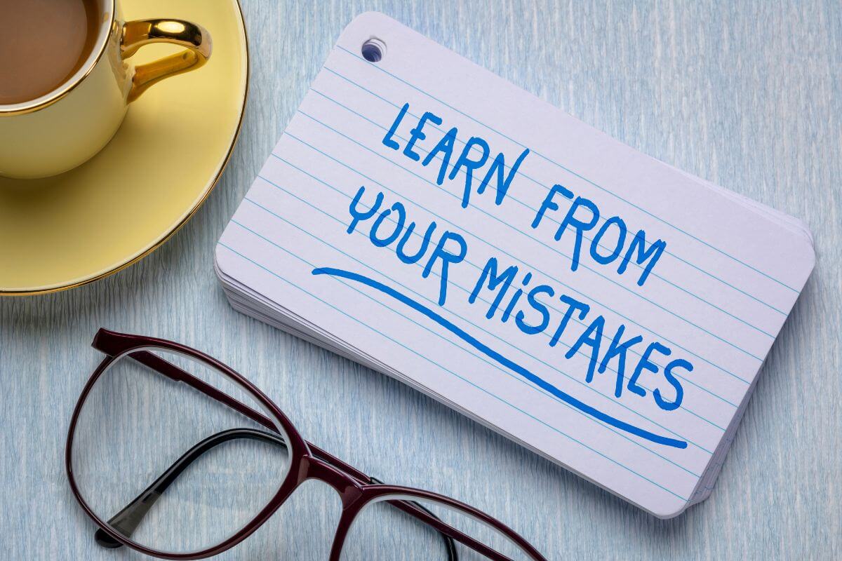 The photo of a coffee, an eyeglass, and papers with notes indicates that learning from your mistakes and moving on helps you leave the past behind while improving.