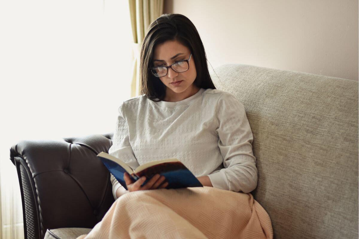 The photo tells about a girl sitting on a couch while reading a book referring to educating yourself on how personal finances can help you make smarter decisions.