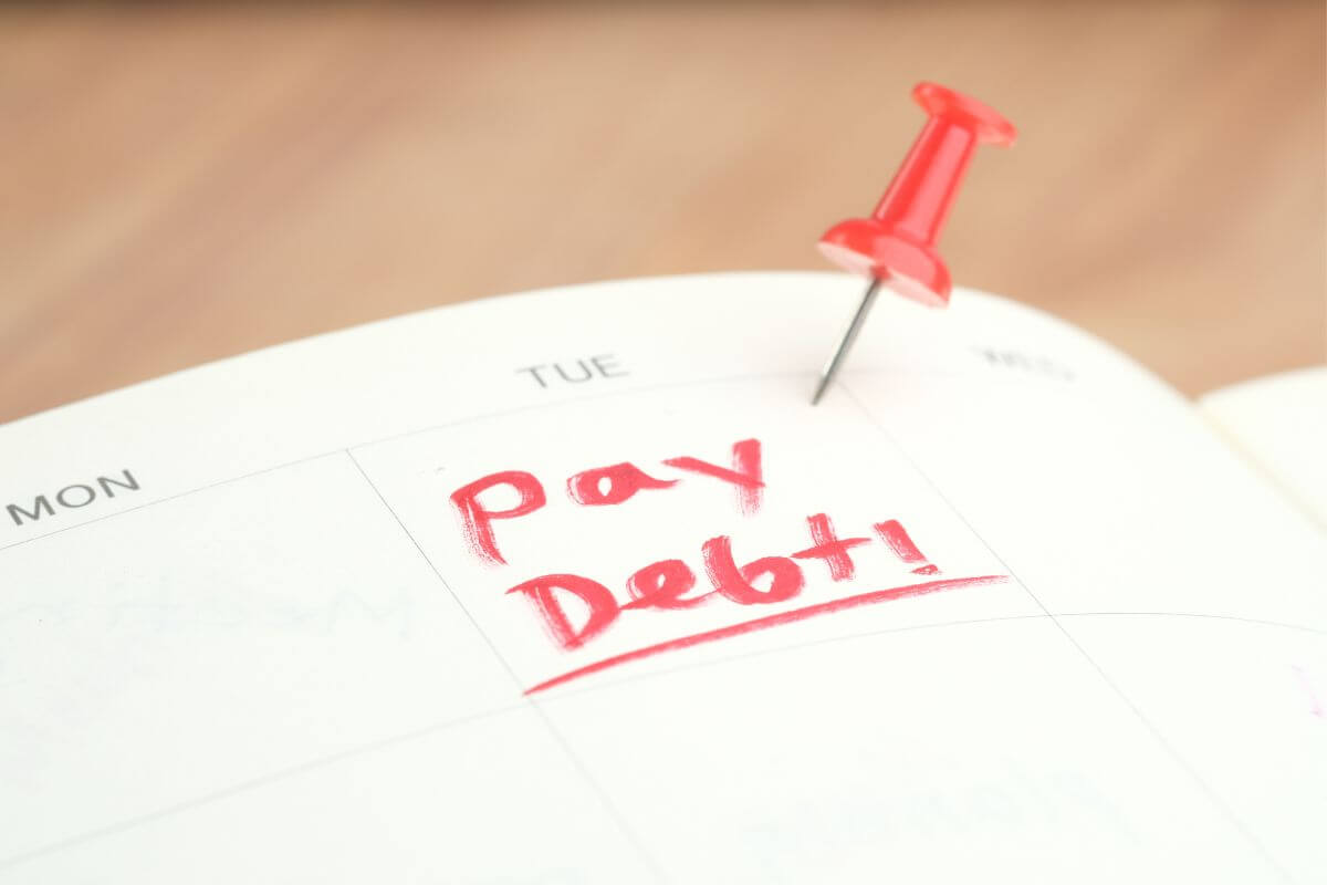 The image of a notebook with a calendar, a pin, and notes indicating that you should prioritize paying off high-interest debt helps reduce how much you pay over time and frees up money for other goals.
