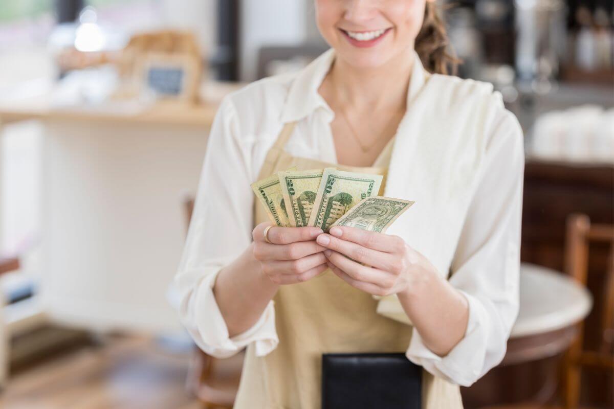 The image shows a waitress counting dollar bills refers to tipping support service workers to supplement low hourly wages, especially in the restaurant and hospitality industries.
