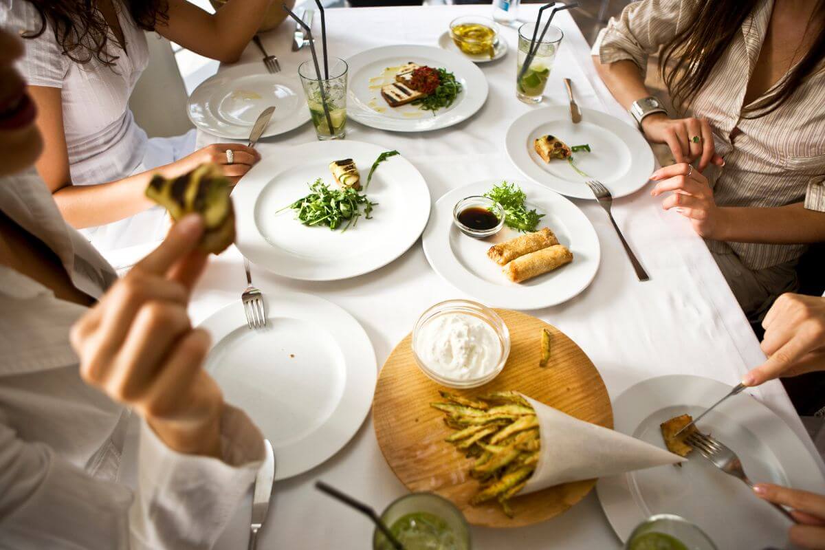 The picture shows a group of people eating at the restaurant which means reflecting on whether dining out is a priority when funds are tight and avoid the added costs of tips.