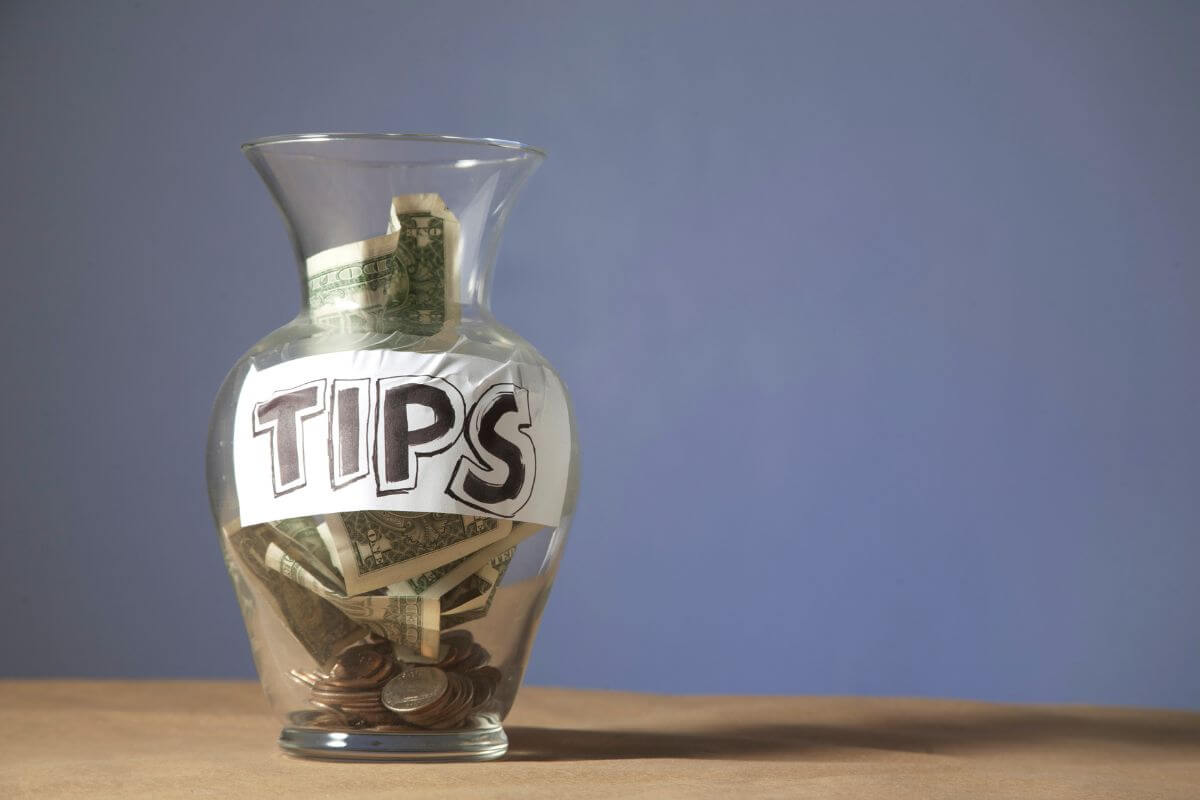 The picture shows a jar filled with dollar bills, and coins, and a note that refers to tipping being eliminated when workers earned higher wages, shifting the responsibility for fair pay to employers could change the way tipping works.