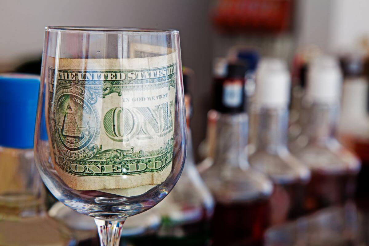 The photo tells about liquors behind and a glass with a dollar bill referring to vast cultural differences in tipping can prevent awkward situations and help you respect local norms.