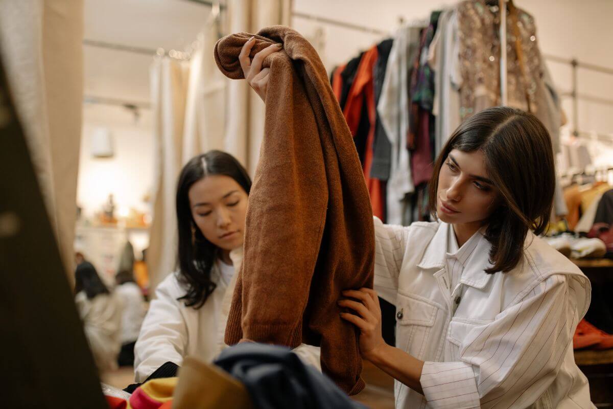 The picture shows women at the thrift store holding clothes which means inspecting items for quality and damage to ensure you got the best quality for your money. 