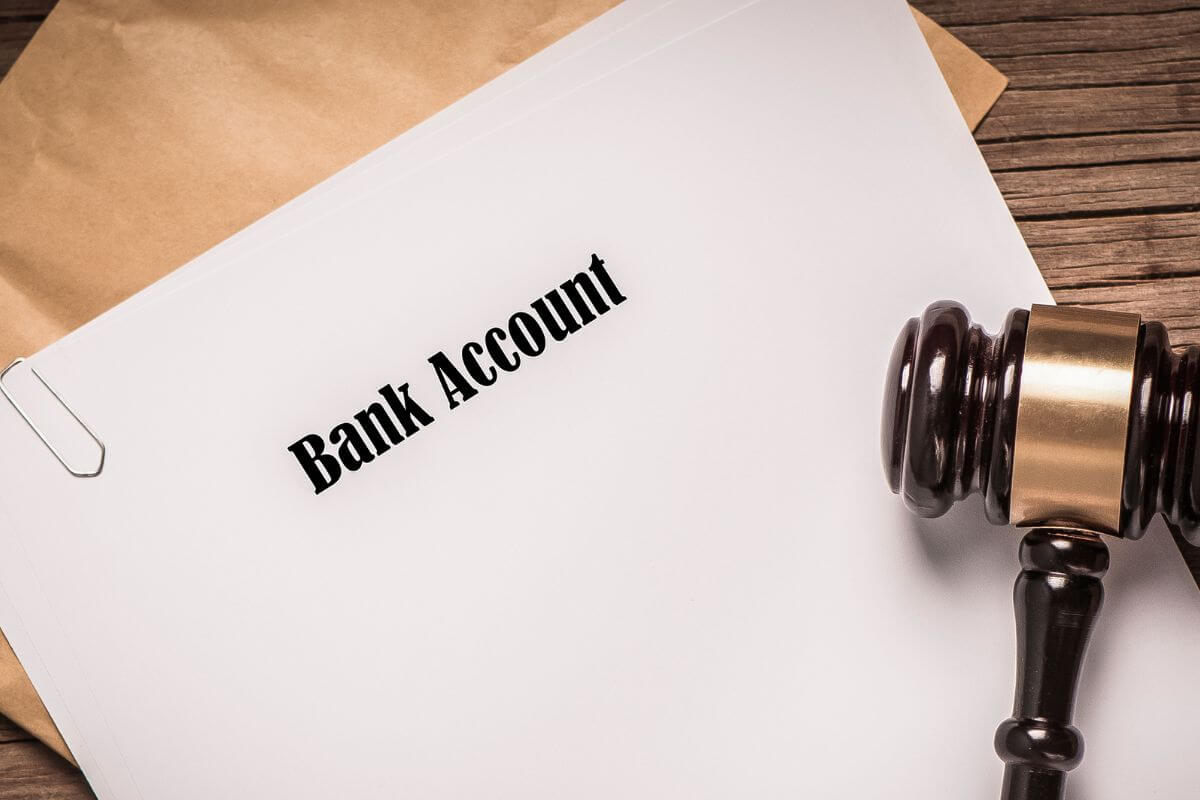 The photo tells about a brown envelope, a gavel, and a piece of paper with notes referring to the use of payable-on-death designations for bank accounts to ensure your intentions are met after you pass.