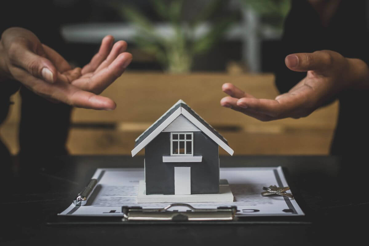 The image shows a clipboard, a miniature house, a key, and two hands pointing it which means using transfer-on-death designations for real estate and vehicles to help your beneficiaries receive assets without probate.