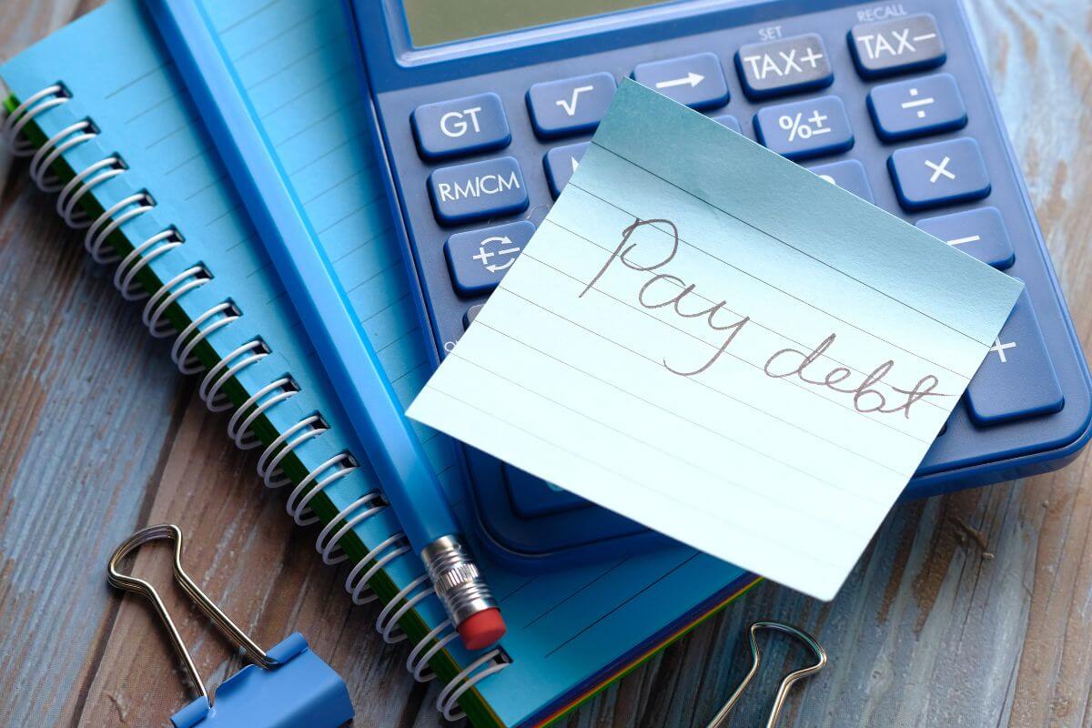 The photo tells about a notebook, a pen, clips, and a piece of paper with notes which means paying off high-interest debt to free up money for retirement, reducing stress, and building financial freedom.