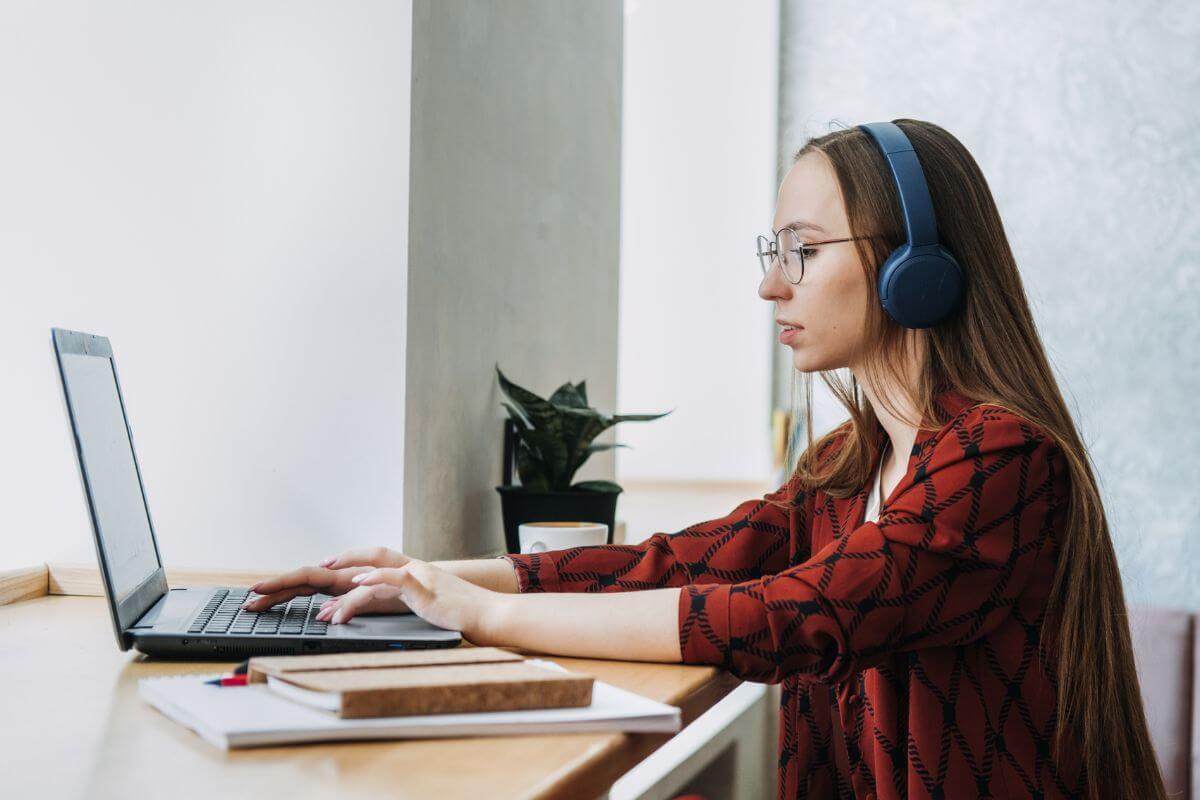 The picture tells about a notebook, papers, and a girl using a laptop with a headset which means focusing on increasing your income through side hustles can help you pay off debt faster or build a bigger retirement fund.