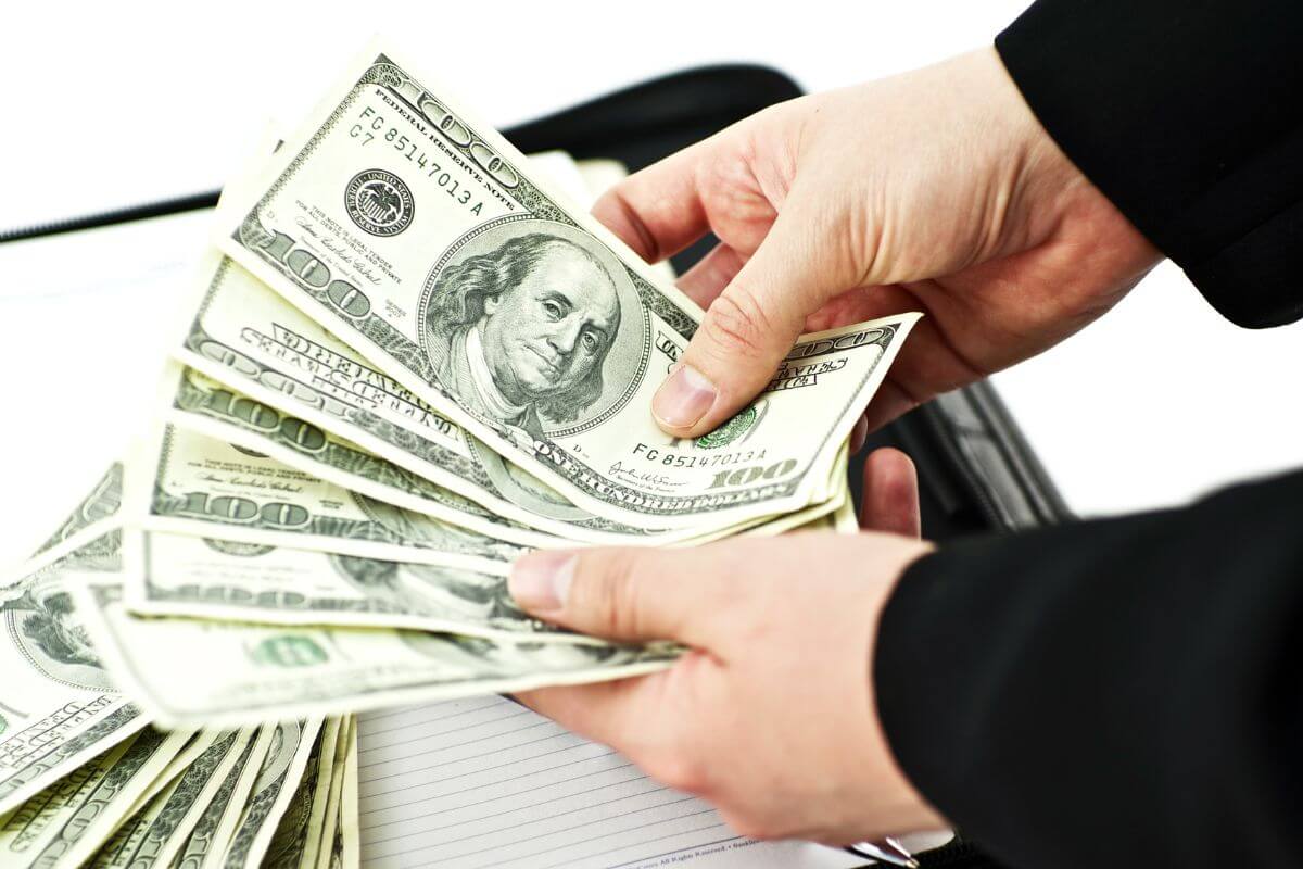The picture of a man's hand counting dollar bills which means to prioritize financial independence over material goods gives you freedom and security in retirement.
