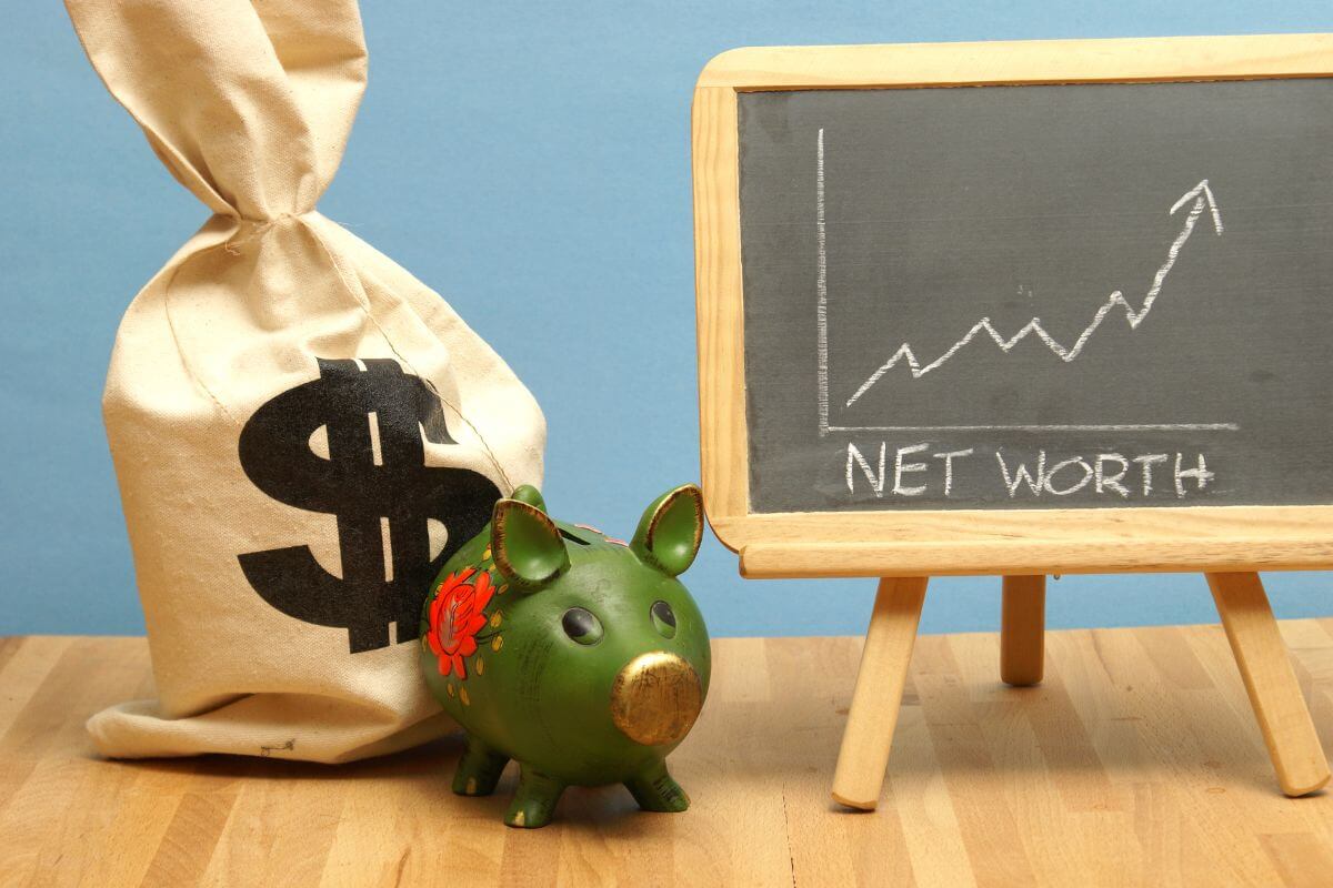 The image shows a bag of cash, a piggy bank, and a blackboard with notes and a rising arrow which means the definition of net worth, understanding it can help you plan for the future and set realistic goals.