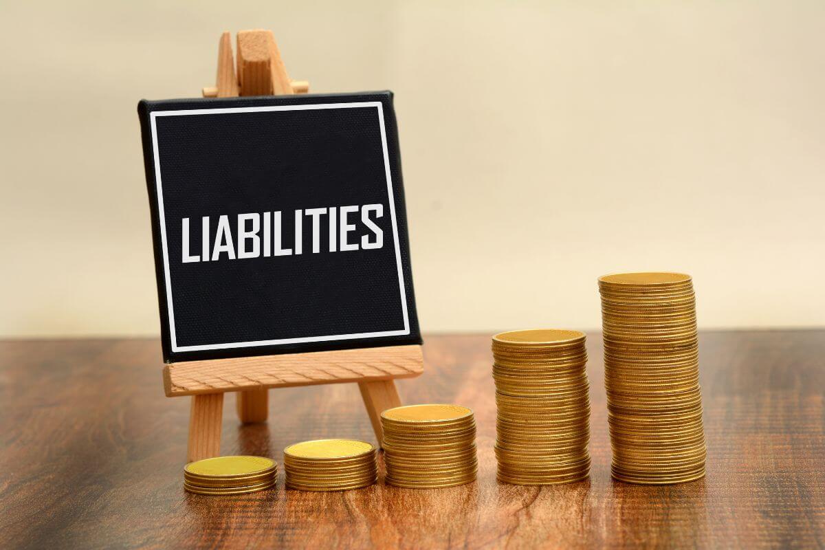 The picture shows stock coins and a mini blackboard with a note which means liabilities are debts or obligations that take money out of your pocket, understanding it can make better decisions.