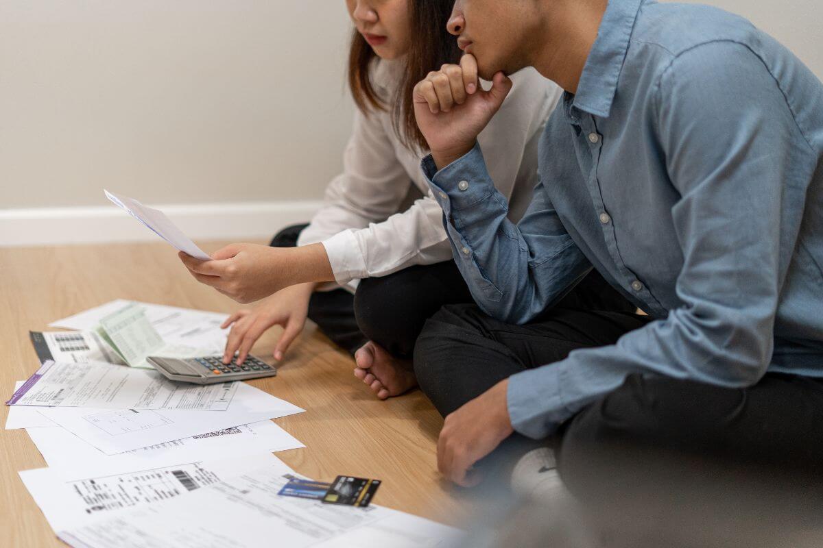 The photo shows credit cards, papers on the floor, and a couple reviewing it and calculating it which means a negative net worth happens when your debts outweigh your assets.