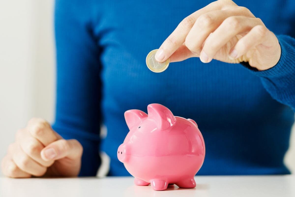 The image shows a small piggy bank and a girl's hand dropping a coin into it referring to start small savings grow over time and can make a huge difference in the long run.
