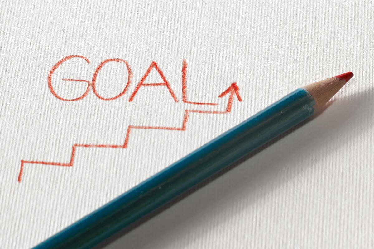 The picture of a pen and a note with a rising arrow which means to consider long-term goals helps you prioritize and build a stronger financial future.