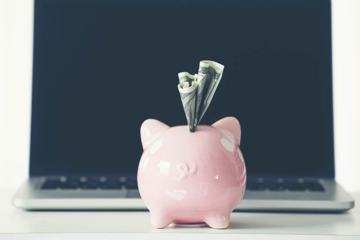 The image of a laptop and a piggy bank with dollar bills refers to automated savings to ensure you save regularly without having to think about it.