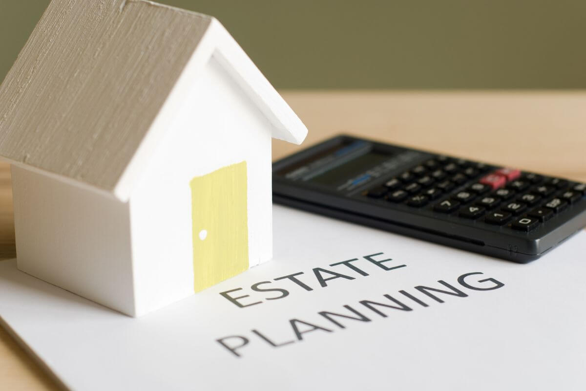 The picture of a calculator, a mini house, and a piece of paper with notes referring to getting your estate planning up to date ensures that your wishes are followed and that no important details are missed.