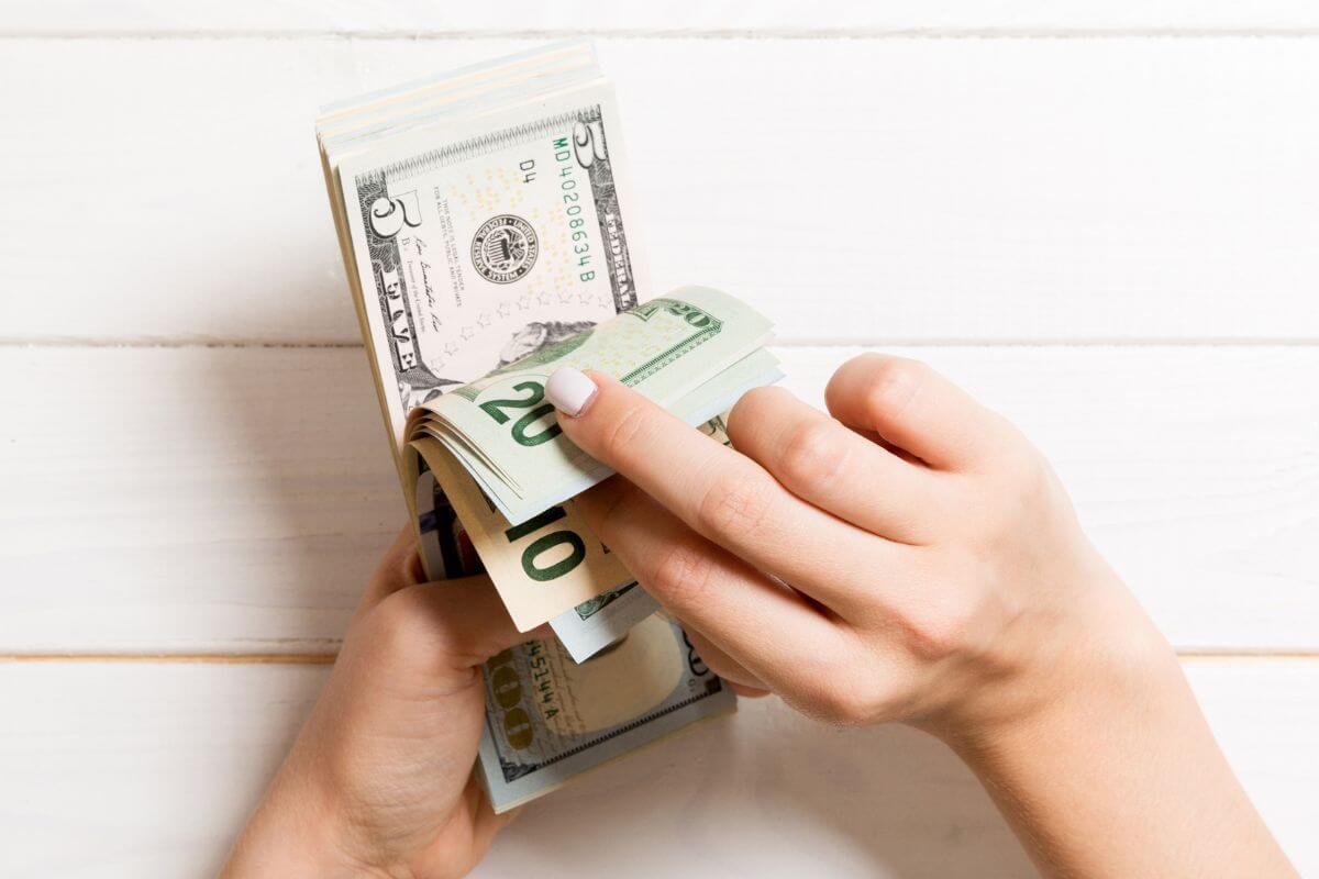 The photo of a girl's hand counting dollar bills referring to getting financially sound ASAP can help create a more secure future.