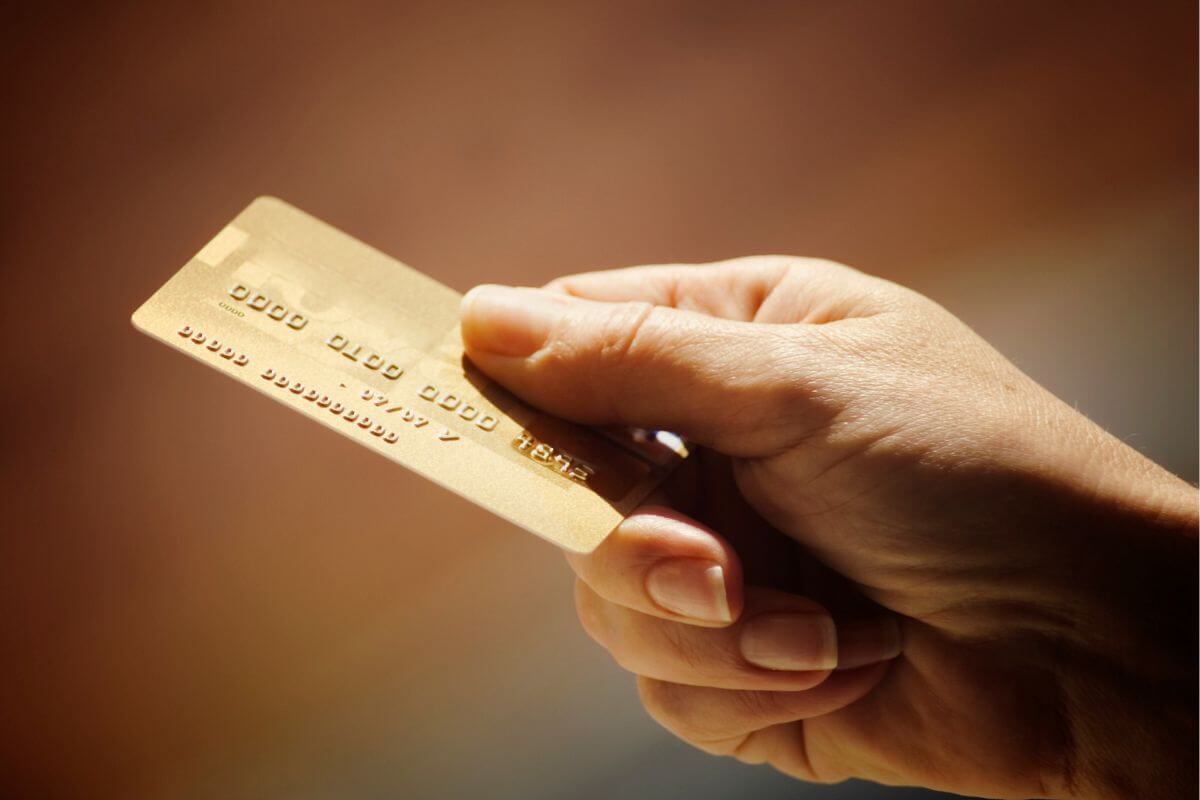The photo tells about a man's hand holding a credit card which means that becoming an authorized user on a family member's credit card can boost your credit.