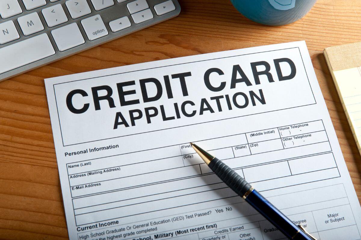 The image shows a keyboard, a notebook, a pen, and a piece of paper with notes referring to avoiding opening multiple credit accounts at once can make lenders see you at risk, focus on opening one account at a time, and using it responsibly.