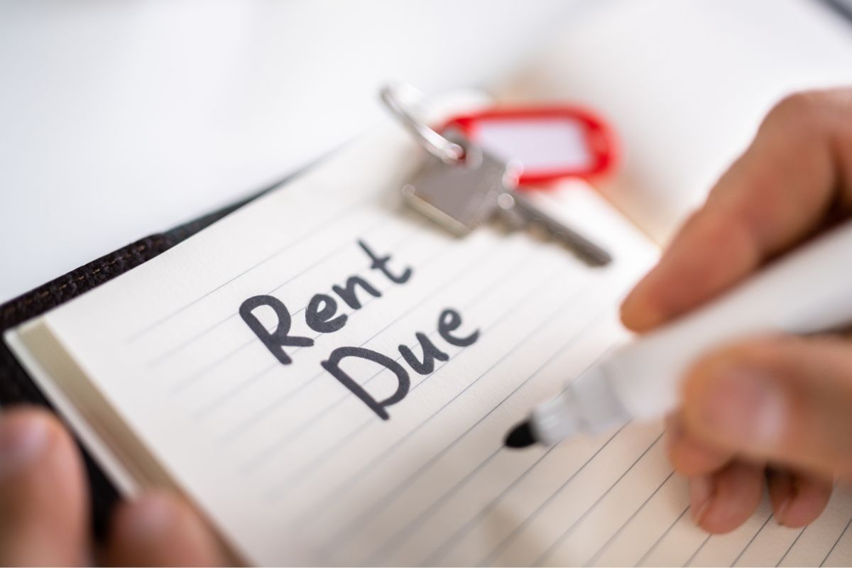 A woman's hand and writing rent due on the notebook.