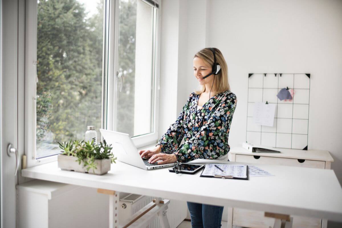 The photo tells about a clipboard, a tablet, a device, a plant, and a girl working on her laptop which means work standing up or while pacing helps you stay alert and engaged.