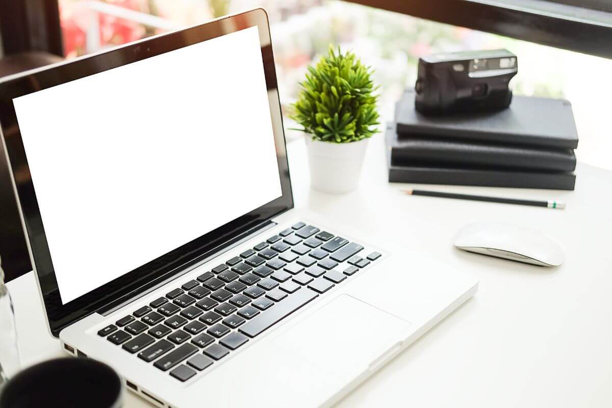 The image of notebooks, a pen, a stapler, a plant, a mouse, and a laptop on the table refers to ending the day by setting your workspace for the next morning helps you start the morning focused and ready to go.