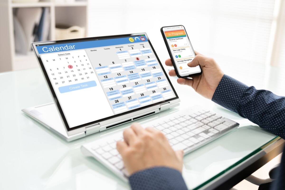 The image tells about a man's hand using a laptop and phone with screen displays which means scheduling time for deep work and turning off all notifications to keep your productivity on track.