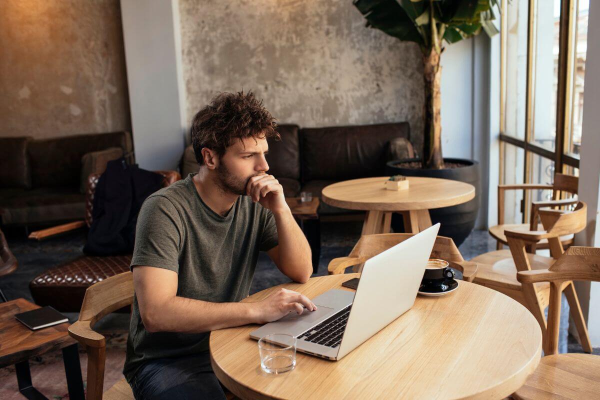 The image shows a man using a laptop while sitting referring to taking on temporary gig work can ringing in extra cash quickly when needed.