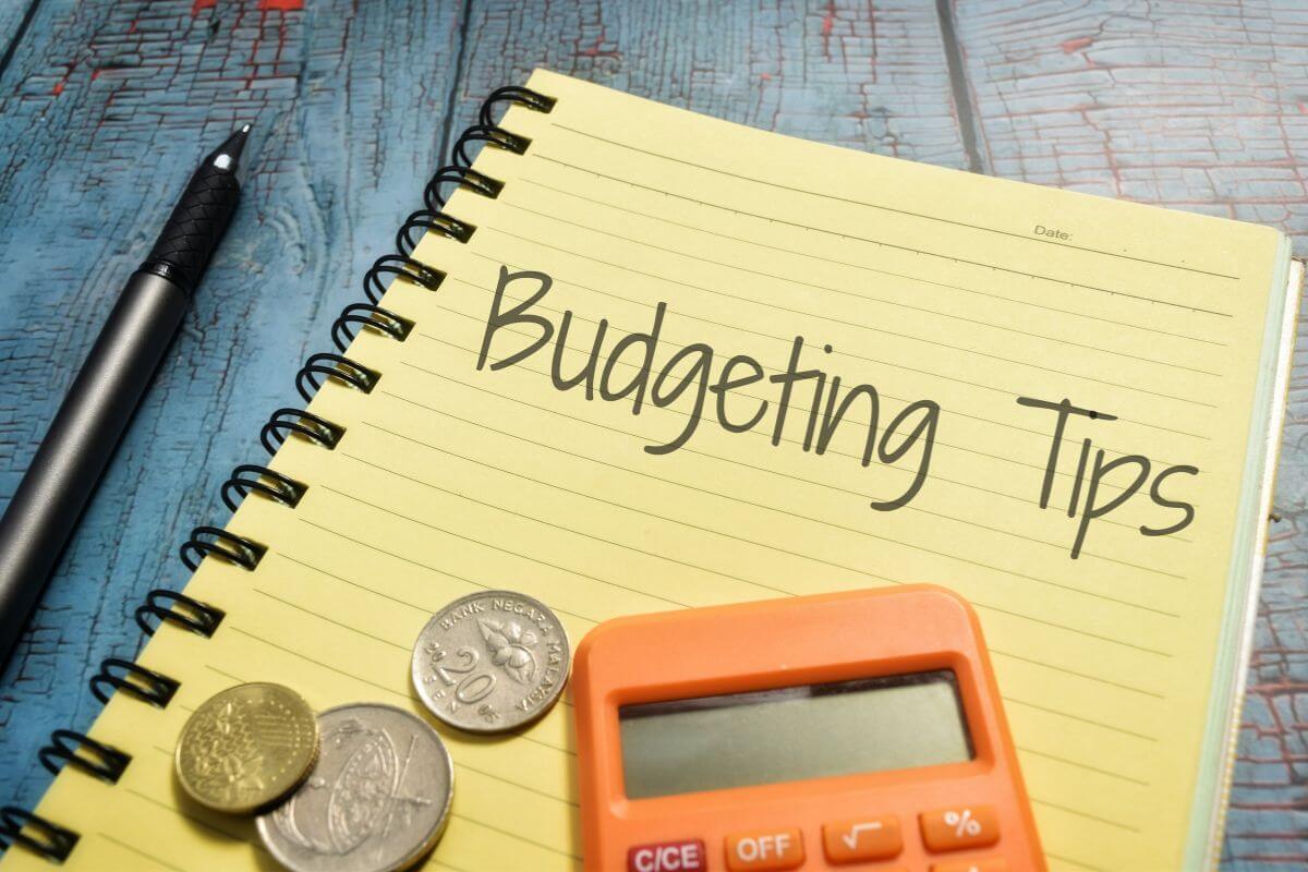 The picture of a pen, coins, a calculator, and a notebook with notes referring to finding more budgeting tips to reduce your expenses helps you feel prepared for uncertain times.