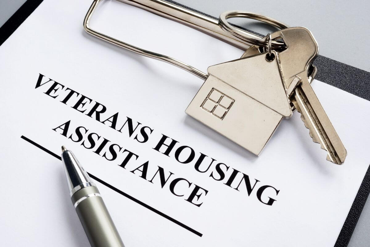 The picture of a clipboard with a piece of paper and notes, a key with a house keychain, and a pen indicating to reach out to local nonprofits for emergency housing assistance that helps with housing costs during tough times.
