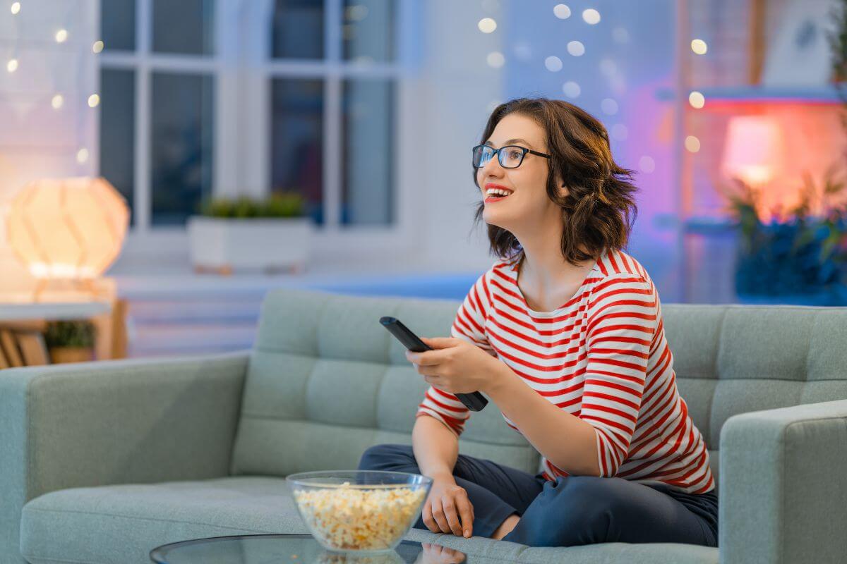 The image shows popcorn on the table and a girl watching  TV with the remote referring to impulse purchases from late-night infomercials that often go unused, avoid these to keep money in your pocket.
