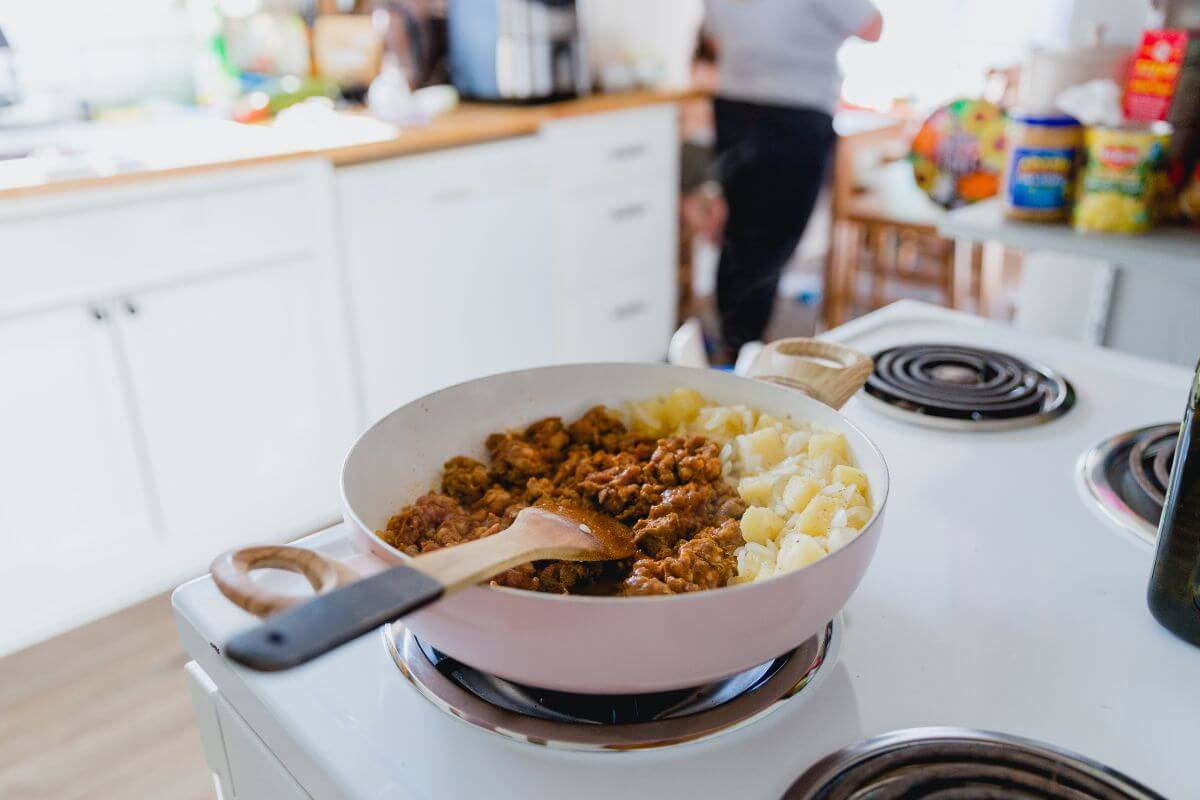 The picture shows a electric stove with a pan, spatula, and cooked food referring to cook all meals at home for a week can show you how much you can save by skipping restaurants.