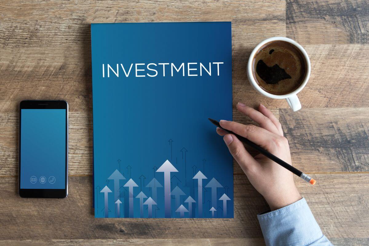 The images show a phone, a coffee, and a man's hand pointing to the book with a title indicating to start an investment portfolio which makes a big difference in long-term financial independence.