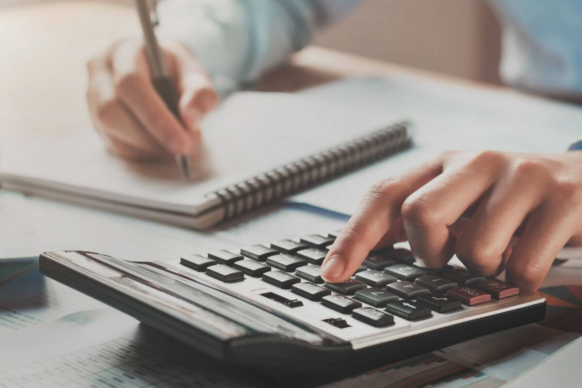 The image shows a man's hand using a calculator and writing in the notebook which means using a simple interest calculator for teenagers to understand the power of compound interest and why starting early matters.