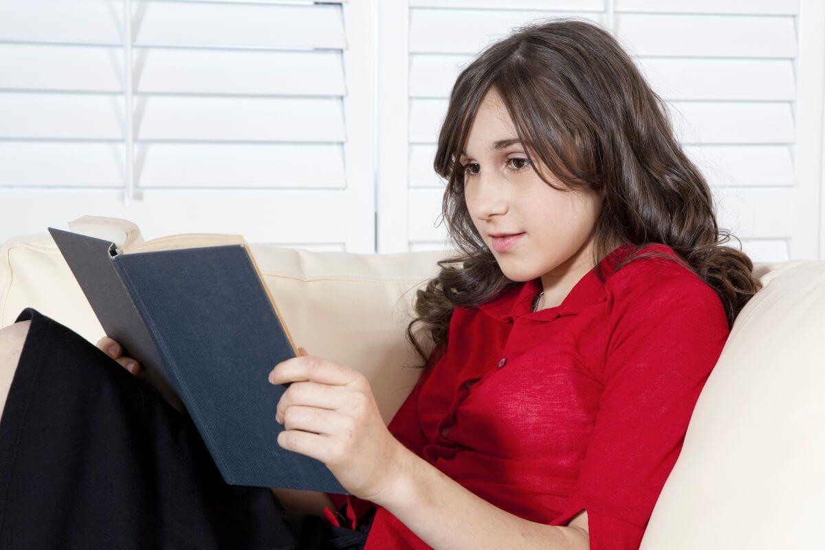 The image shows a girl reading a book which means reading books on personal finance gives teens practical advice they can use right away.