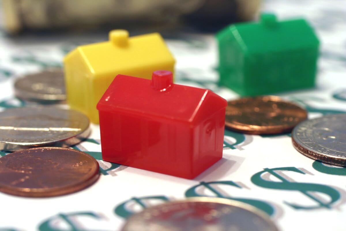 The image shows a mini house figure, coins, and paper with dollar signs referring to play board games like monopoly helps focus on managing money and makes learning about finances fun.