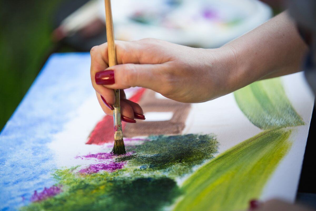 The image shows a girl's hand holding a brush painting the canvas referring to turning hobbies into multiple income streams to build wealth while doing what you enjoy.