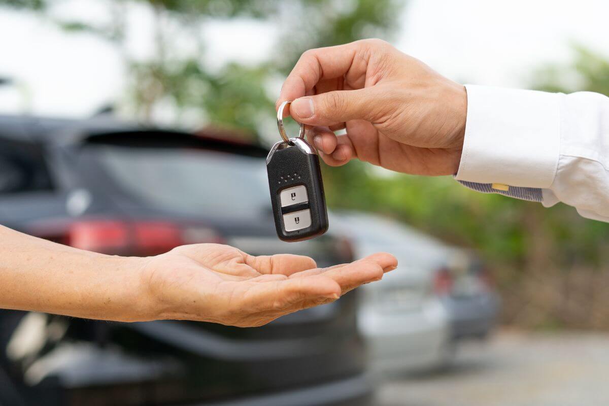 The image tells about a car behind, a man's hand with a polo giving the key car to the man's hand which means to rent out your car when you're not using it helping you earn without extra effort.