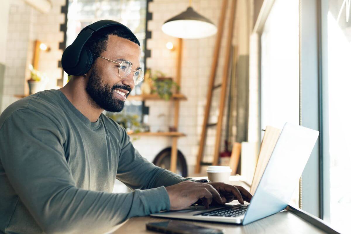 The photo shows a man using a laptop with a headset which means that taking on remote work can save more while still enjoying a comfortable lifestyle.