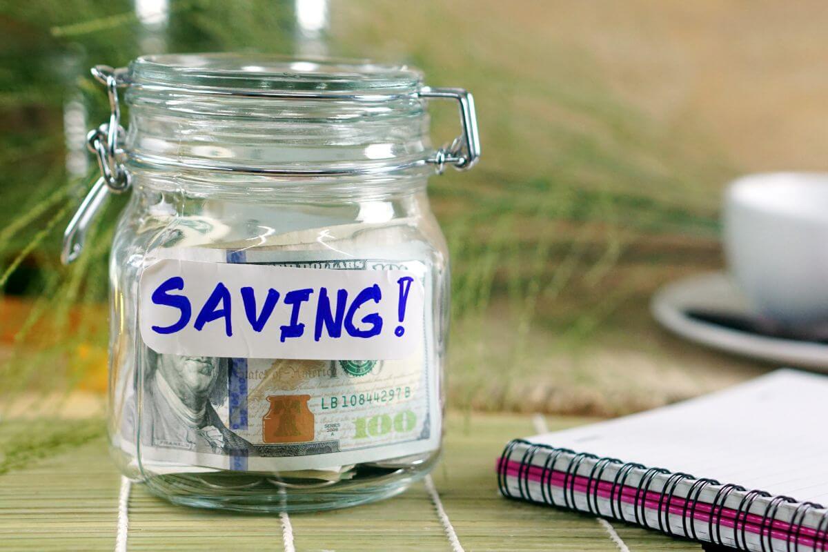 The image of a notebook and a jar with dollar bills and a note indicating to commit to earning and saving your next pay keeps you from falling into the lifestyle inflation trap.