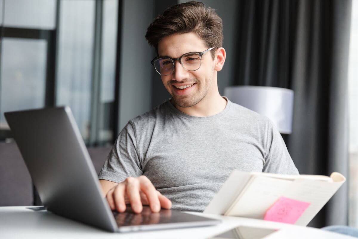 The image tells about a man using a laptop while holding papers indicating that learning your FI number keeps you focused and motivated on the road to freedom.
