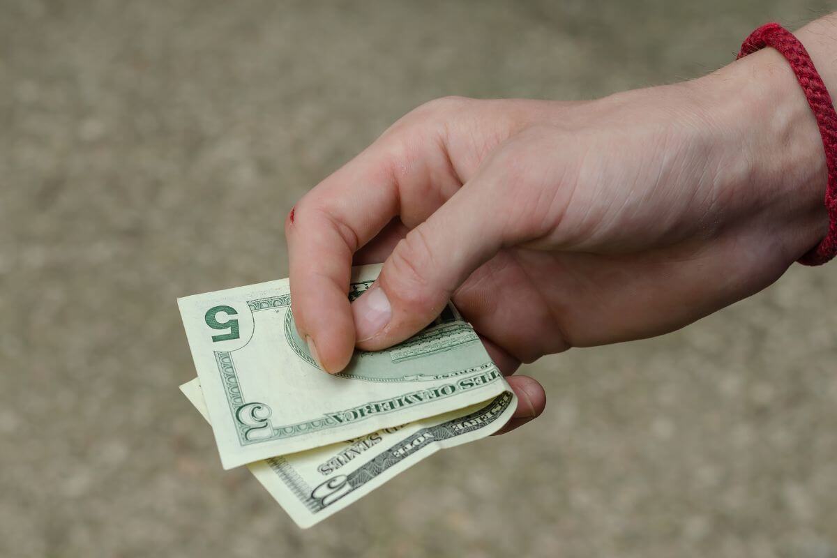The picture shows a man's hand to holding a $5 bill which means save every $5 bill you touch and put it in a jar and let it add up over time.