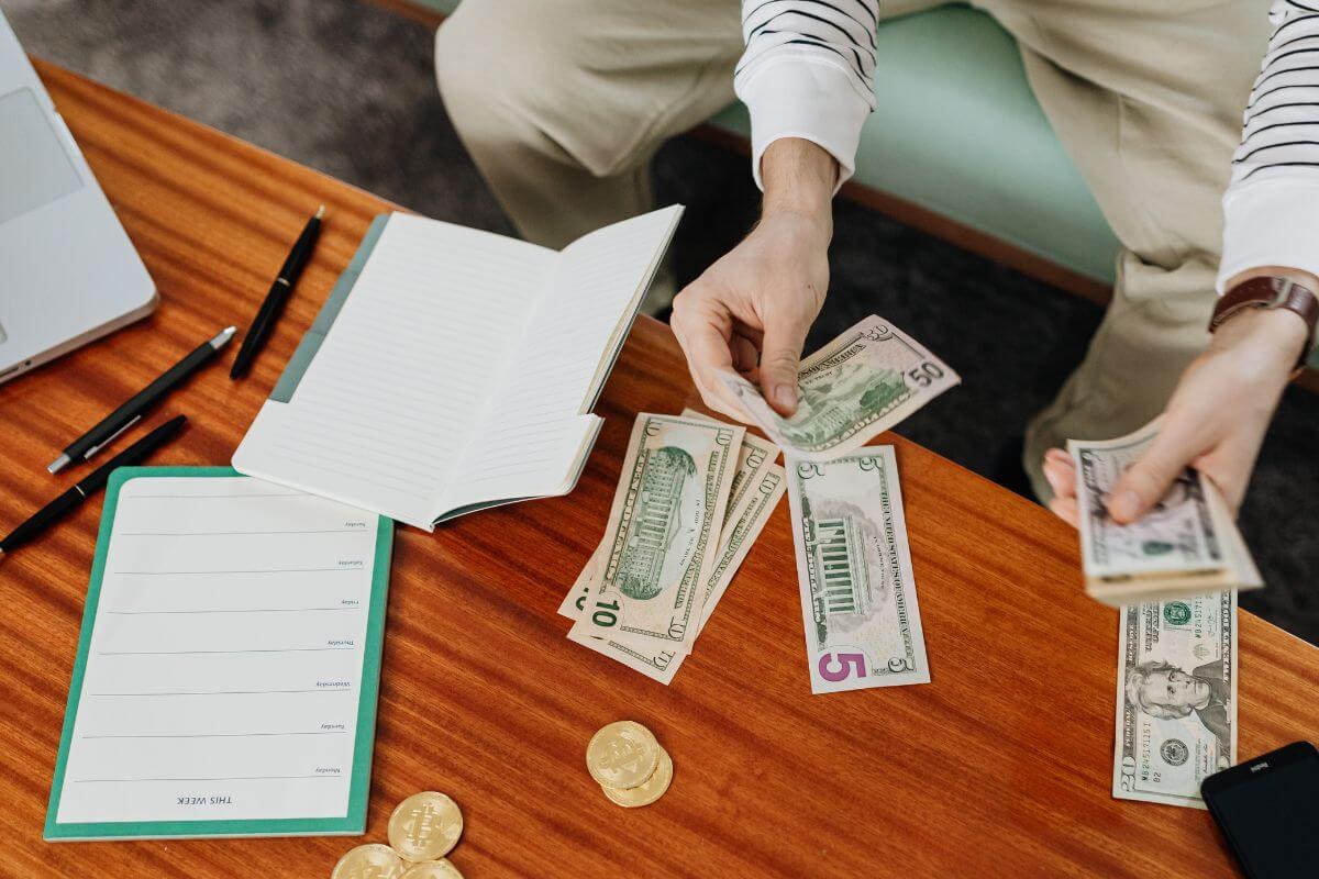 The picture tells about notebooks, pens, coins, and a man grouping the dollar bills which means creating a fun cap budget that keeps you from going overboard while still allowing for some enjoyment.