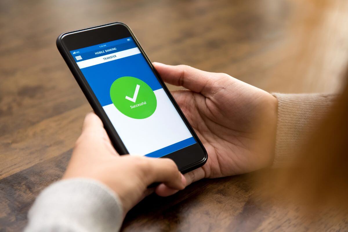 The image shows a girl's hand using a phone with a screen display referring to setting up an automatic transfer to savings to build your savings without even thinking about it.