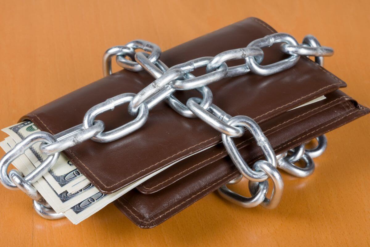 The picture of a wallet with dollar bills and chains referring to living like you're broke helps you save more by focusing on needs over wants.