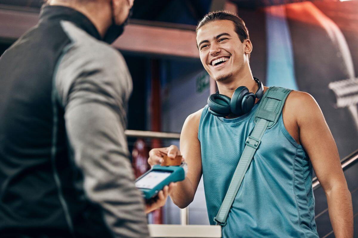 The image shows a coach holding a machine swipe and a man with a bag and headset inserting his card into it, which means negotiating every single bill helps you save money on recurring expenses, and the savings can add up quickly over time.