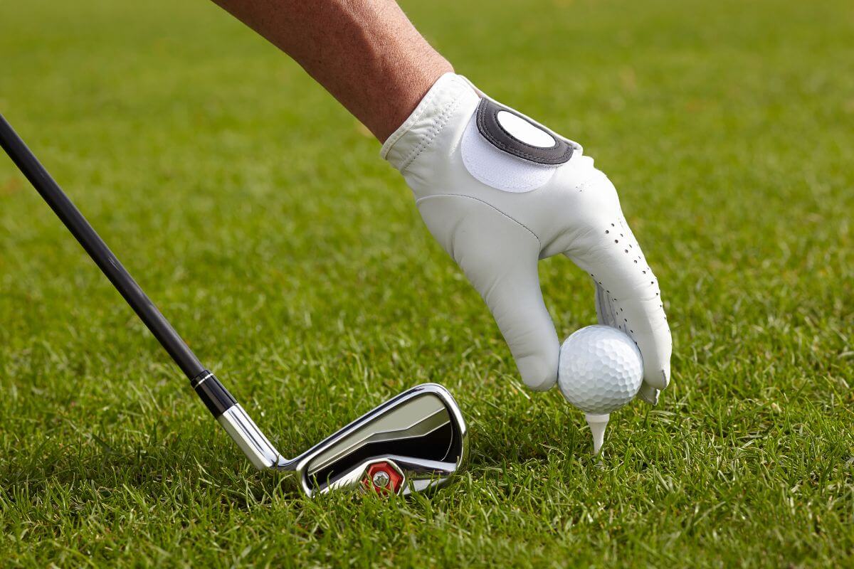 The image shows a man's hand placing the ball and holding a stick which means that working as a golf caddy at a high-end course can pay very well with tips, which is a relaxed job that lets you spend time outdoors.