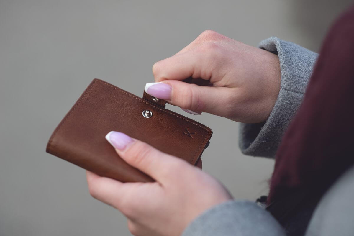 The picture of a girl's hand closing her wallet means implementing a buy nothing month to cut spending and makes you more aware of what you truly need.