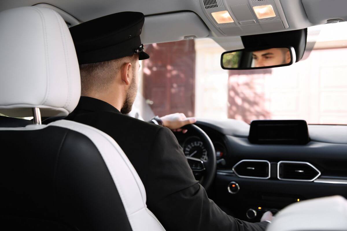 The photo shows a man in a suit driving a car which means becoming a luxury RV delivery driver pays well and offers a relaxing space.
